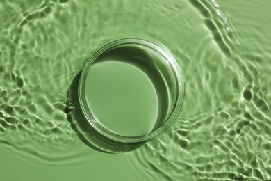 Photo of Stylish presentation for product. Glass podium in water on pale green background, top view