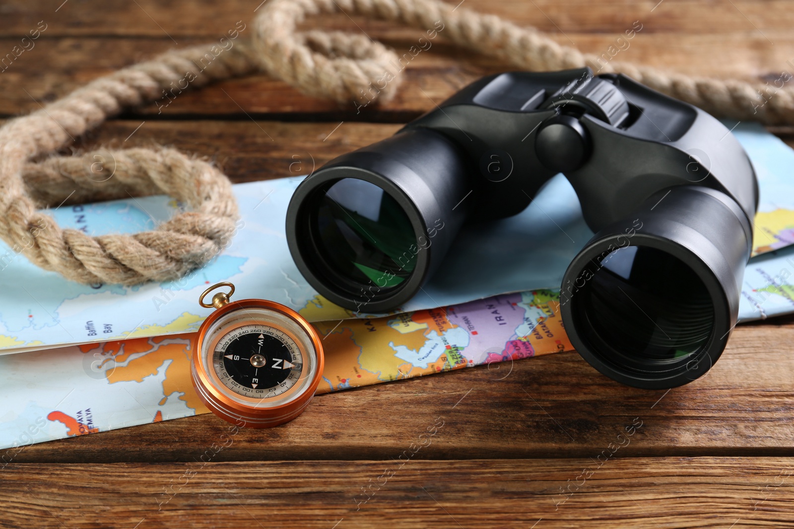 Photo of Modern binoculars, map, compass and rope on wooden table, closeup