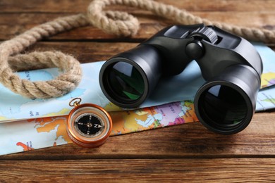 Modern binoculars, map, compass and rope on wooden table, closeup