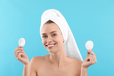Photo of Removing makeup. Smiling woman with cotton pads on light blue background