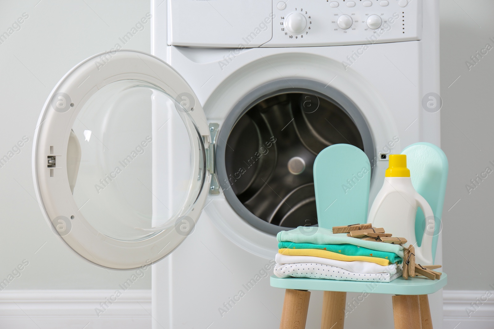 Photo of Bottle of detergent and children's clothes on chair near washing machine