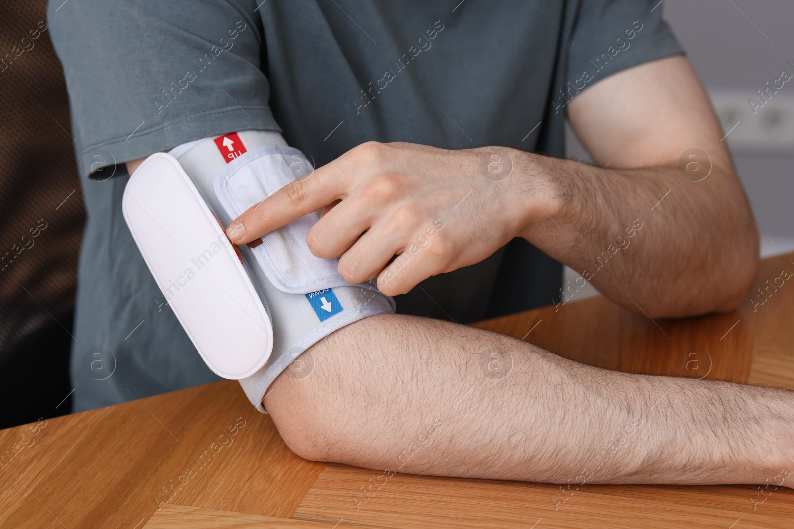 Photo of Man measuring his blood pressure with tonometer at wooden table indoors, closeup