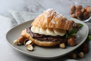 Photo of Delicious croissant with banana, chocolate and hazelnuts on gray table, closeup