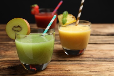 Delicious colorful juices in glasses on wooden table, closeup