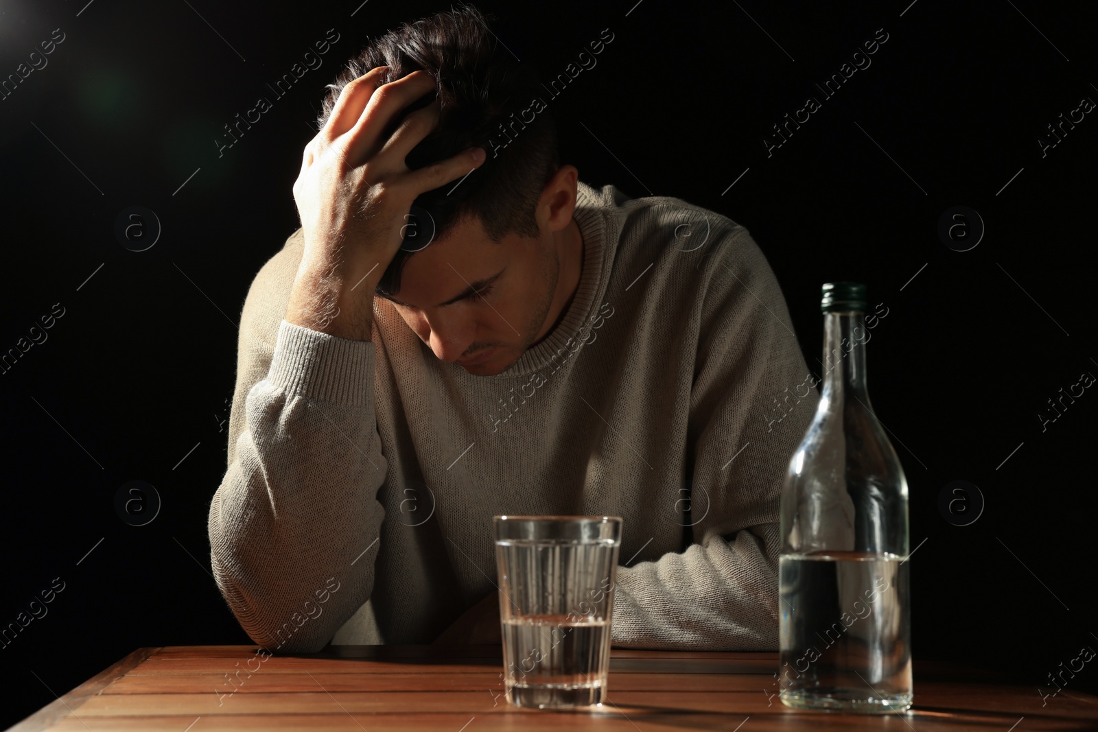 Photo of Addicted man with alcoholic drink at wooden table against black background