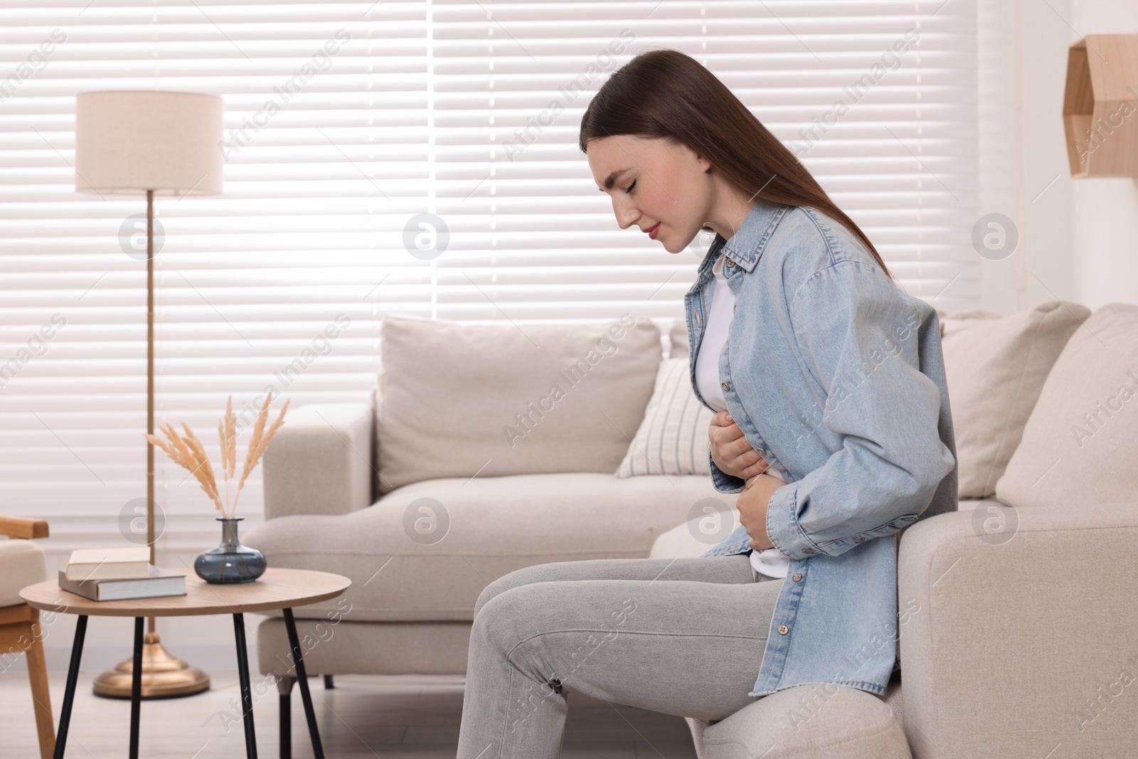 Photo of Young woman suffering from stomach pain at home