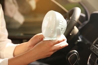 Photo of Woman with portable fan in car on hot summer day, closeup