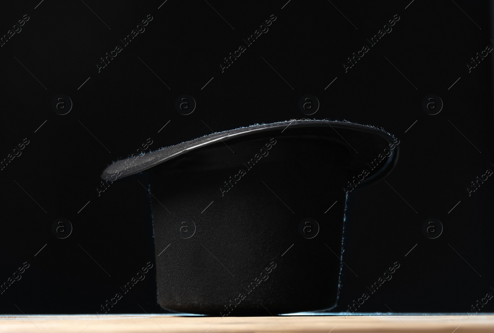 Photo of Magician's hat on wooden table against black background