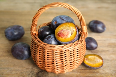 Photo of Delicious ripe plums in wicker basket on wooden table