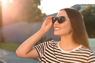 Beautiful smiling woman in sunglasses outdoors, space for text