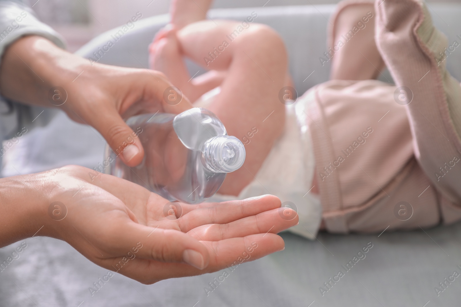 Photo of Mother with bottle of massage oil near baby on changing table indoors, closeup