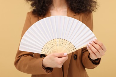 Photo of Woman holding hand fan on beige background, closeup