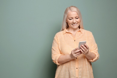 Photo of Mature woman using mobile phone on color background