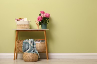 Photo of Console table with decor and beautiful hortensia flower near light green wall in hallway, space for text. Interior design