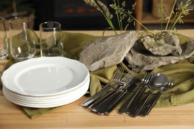 Photo of Clean dishes, stones and plants on wooden table in dining room, closeup