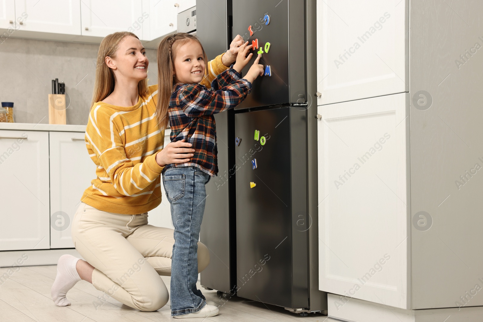 Photo of Mom and daughter putting magnetic letters on fridge at home. Learning alphabet