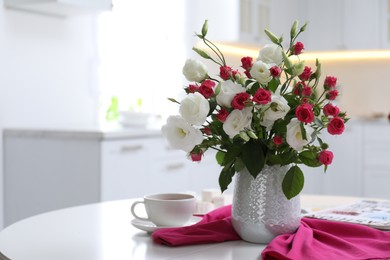 Vase with fresh flowers and cup on table in kitchen. Space for text