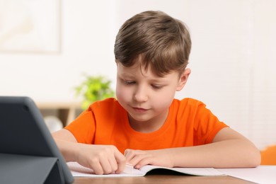 Photo of Little boy erasing mistake in his notebook at wooden desk indoors