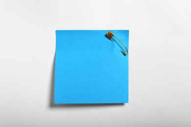 Photo of Blue paper note attached with safety pin to white background, top view