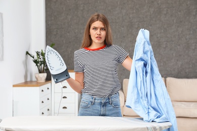 Photo of Emotional woman with iron and shirt at home