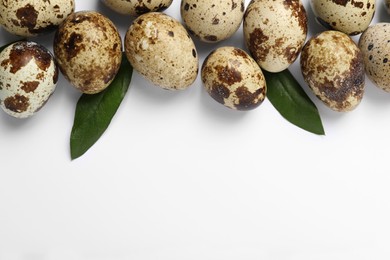 Photo of Speckled quail eggs and green leaves on white background, flat lay. Space for text