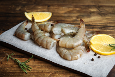Photo of Fresh raw shrimps with lemon and rosemary on wooden table, closeup