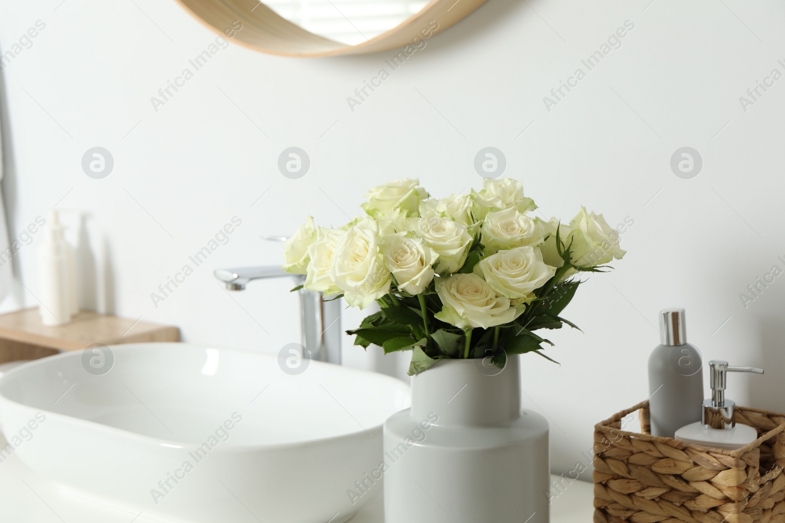 Photo of Vase with beautiful white roses and toiletries near sink in bathroom