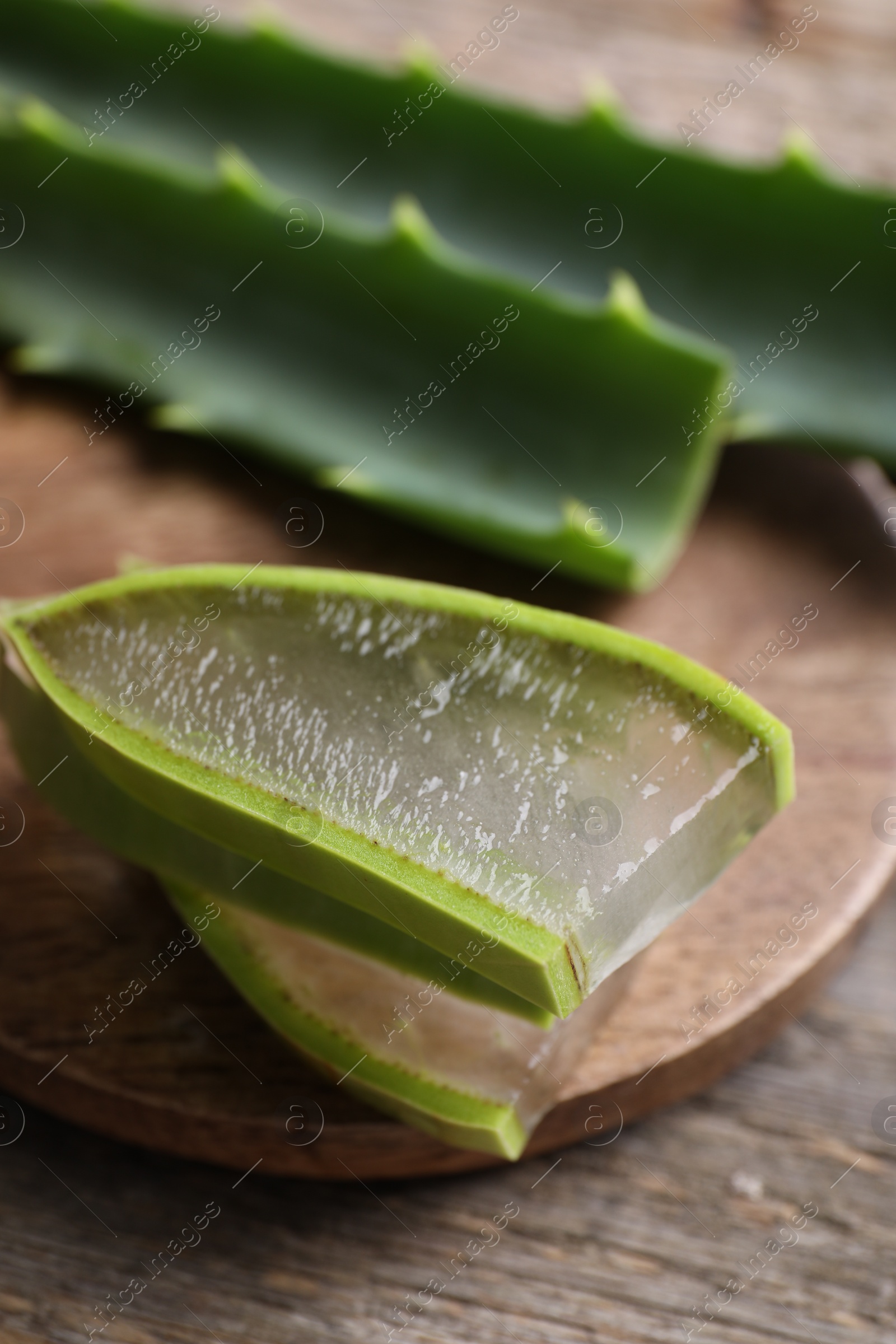 Photo of Slices of fresh aloe vera leaves with gel on wooden table, closeup