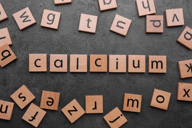 Photo of Word Calcium made of wooden cubes with letters on black background, top view