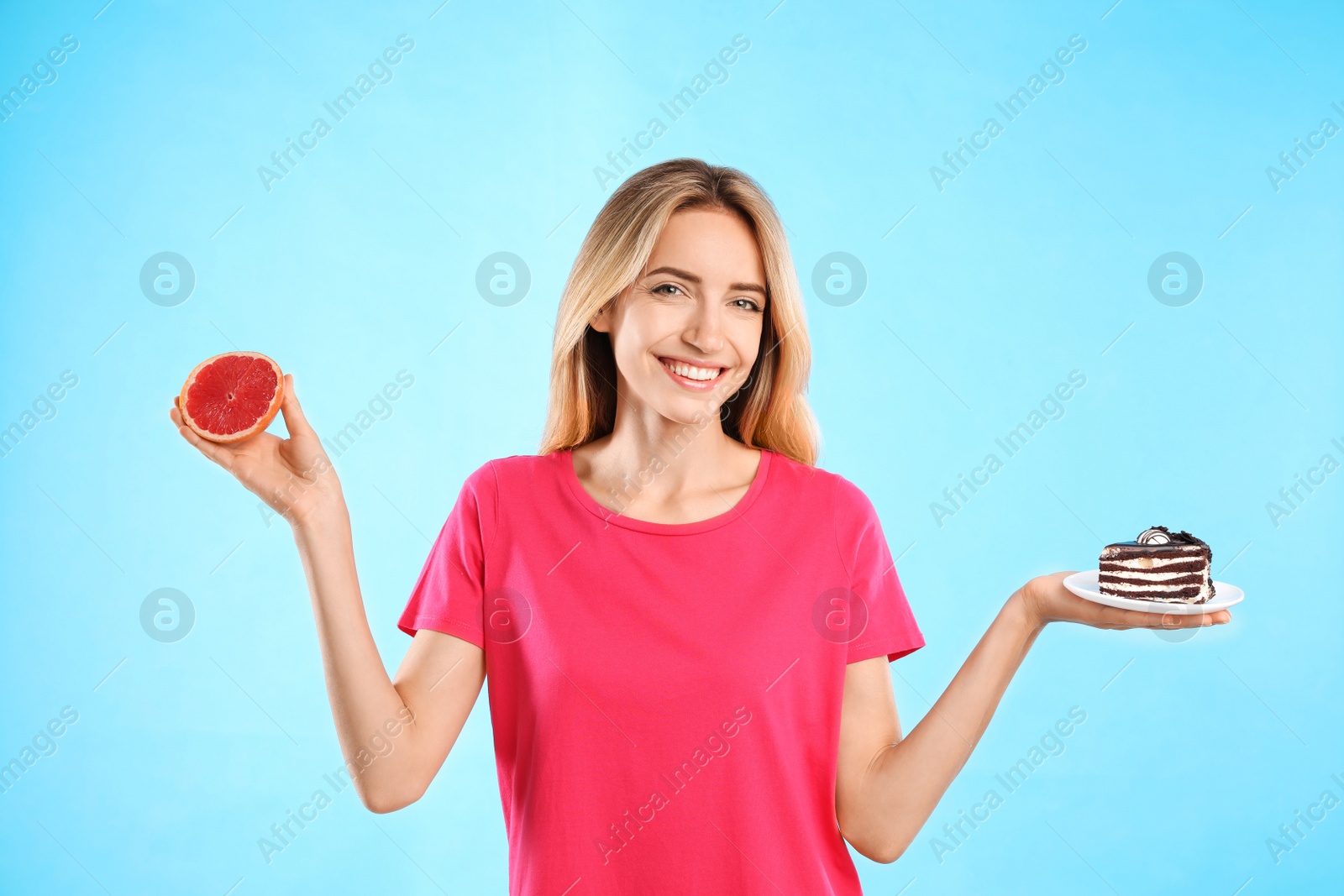 Photo of Woman choosing between cake and healthy grapefruit on light blue background