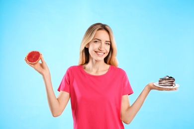 Photo of Woman choosing between cake and healthy grapefruit on light blue background