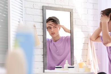 Photo of Teenage boy with acne problem looking in mirror at home