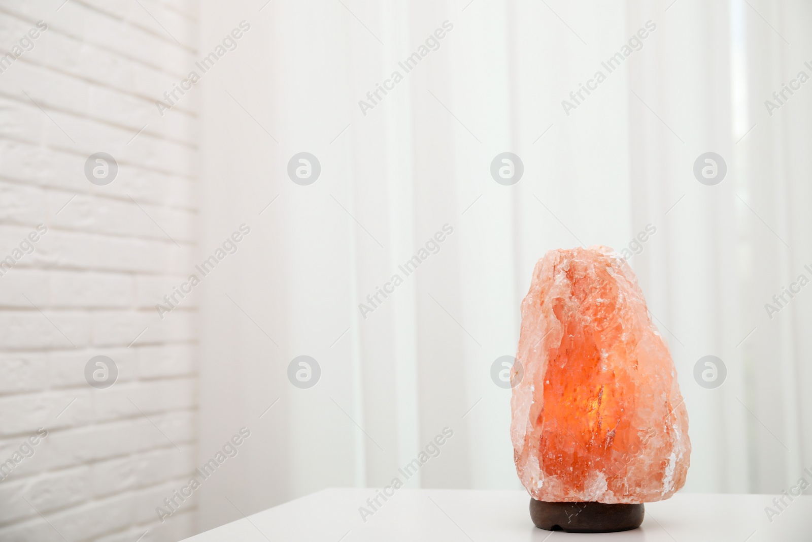 Photo of Himalayan salt lamp on white table indoors. Space for text