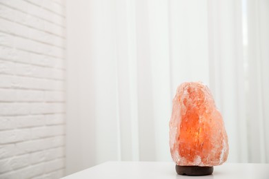 Photo of Himalayan salt lamp on white table indoors. Space for text