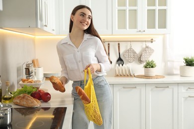 Woman holding string bag with baguettes in kitchen