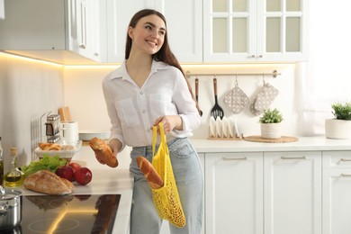 Photo of Woman holding string bag with baguettes in kitchen