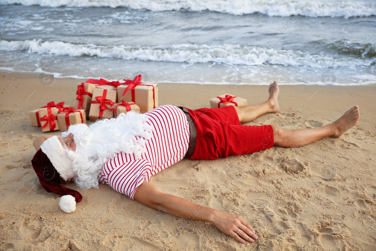 Photo of Santa Claus with presents relaxing on beach. Christmas vacation