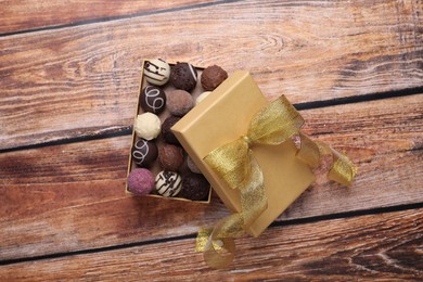 Photo of Open box with delicious chocolate candies on wooden table, top view