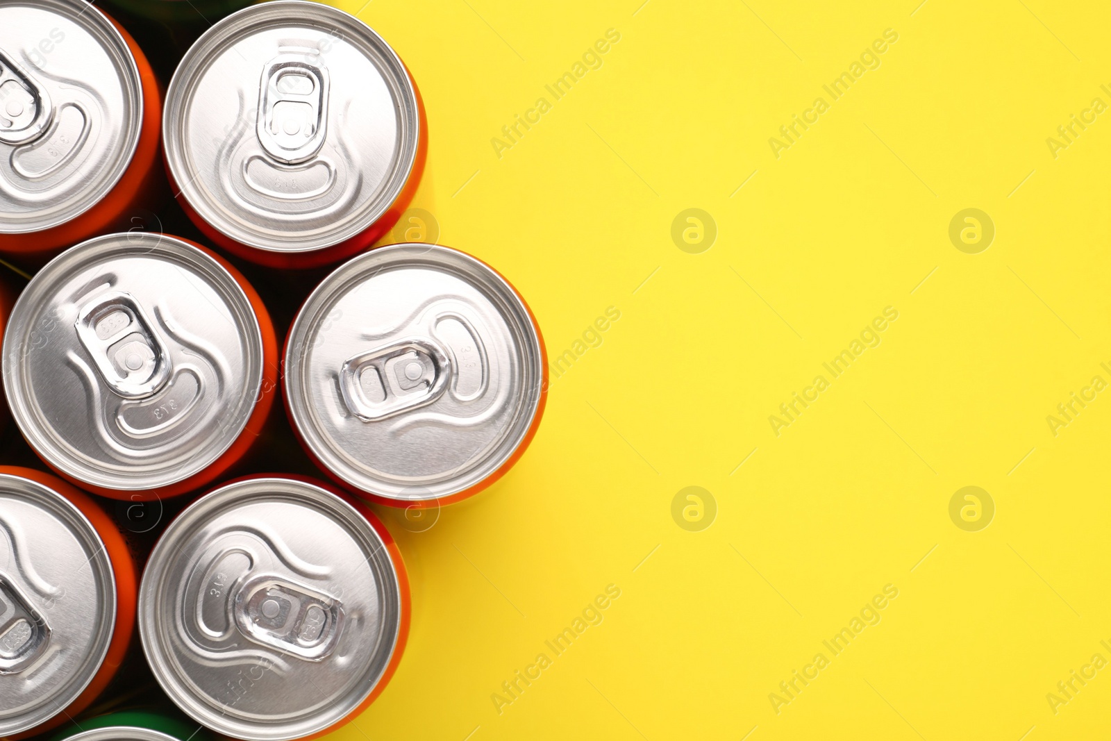 Photo of Energy drink in cans on yellow background, top view. Space for text