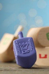 Hanukkah celebration. Dreidels with jewish letters on wooden table against blurred lights, closeup