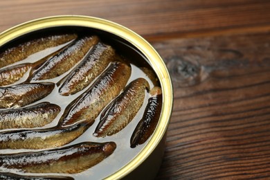 Open tin can of sprats on wooden table, closeup