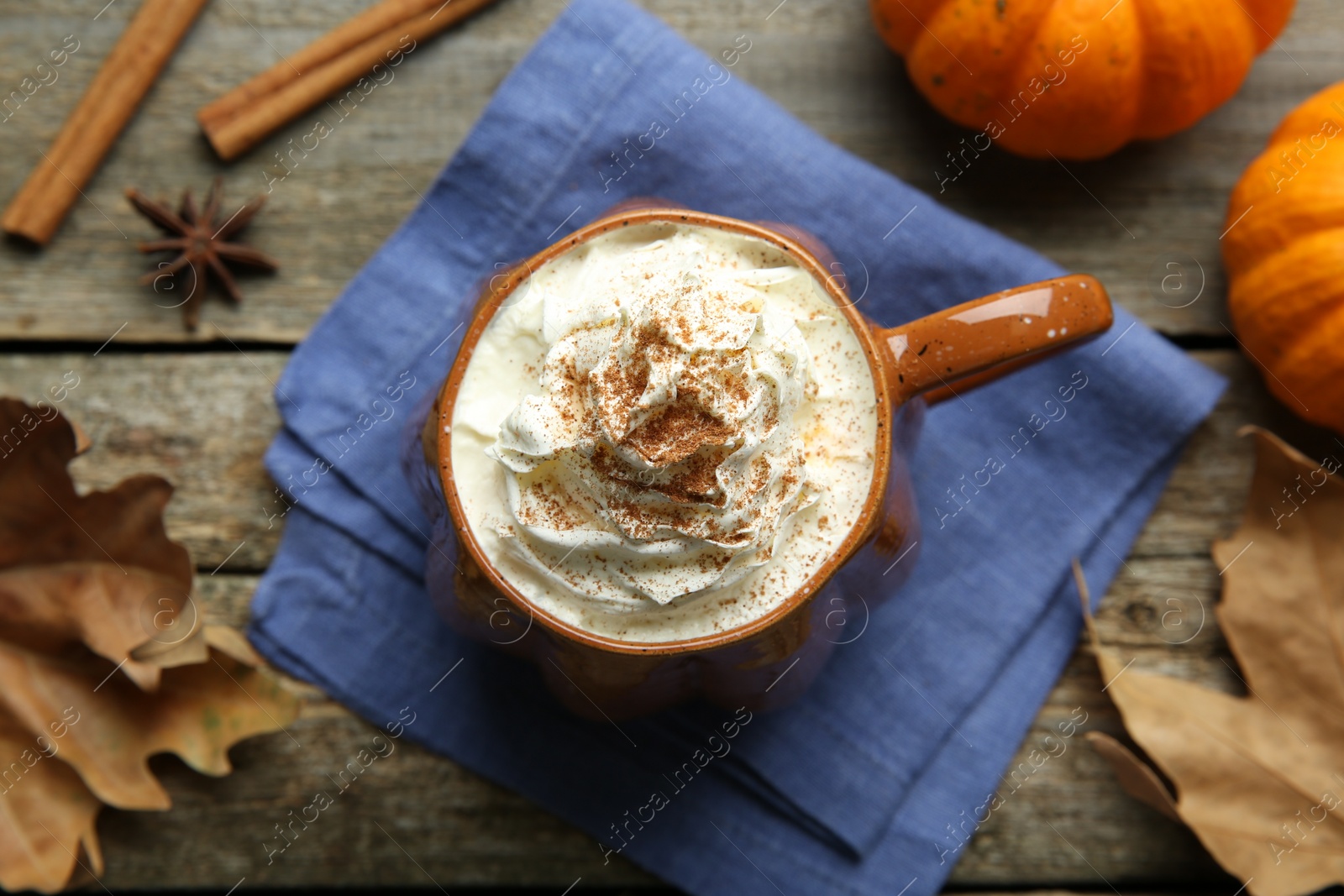 Photo of Mug of pumpkin spice latte with whipped cream, ingredients and dry leaves on wooden table, flat lay