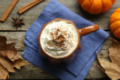 Photo of Mug of pumpkin spice latte with whipped cream, ingredients and dry leaves on wooden table, flat lay