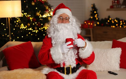 Merry Christmas. Santa Claus with cup of drink watching TV on sofa at home