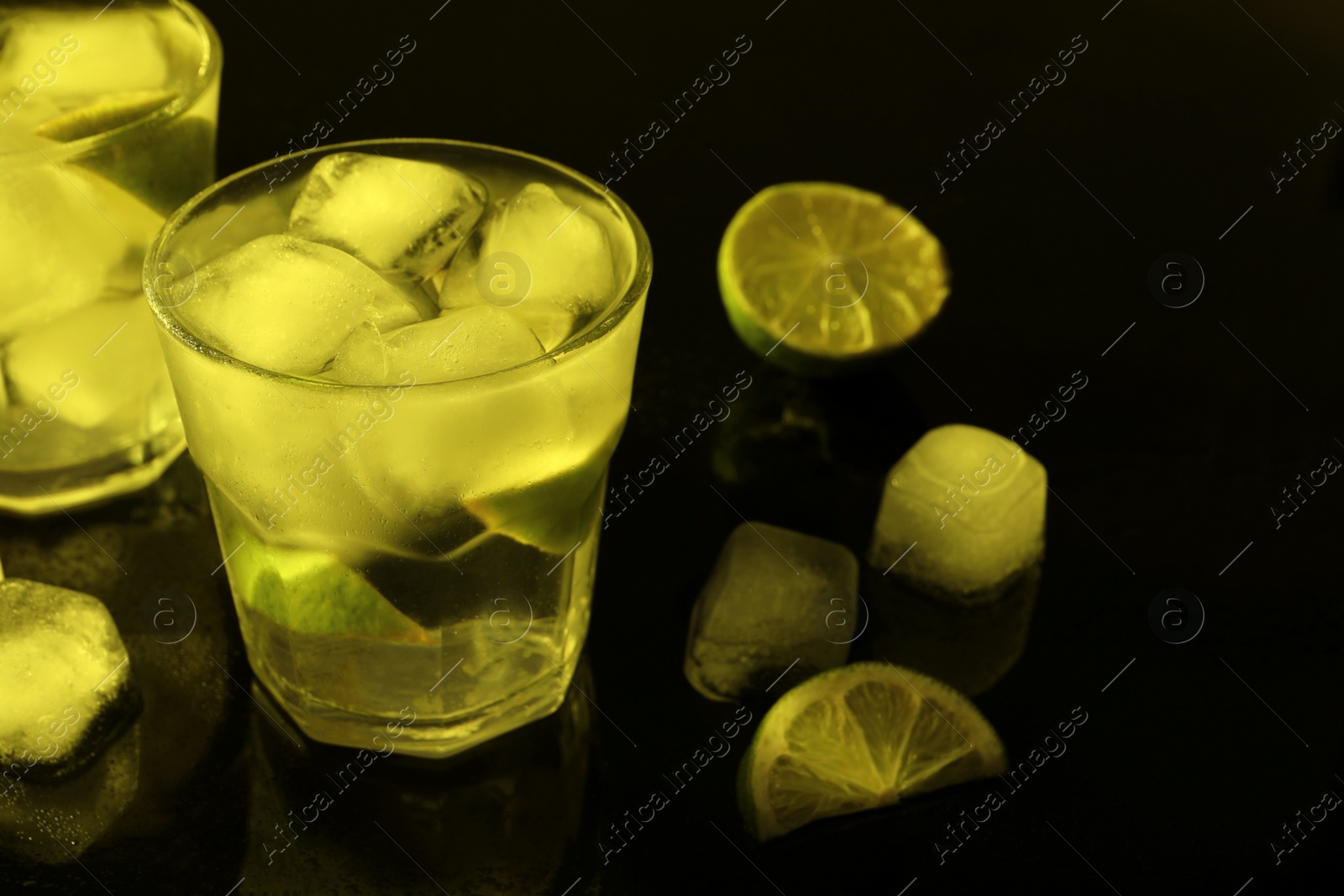 Photo of Shot glasses of vodka with ice cubes and lime slices on dark background