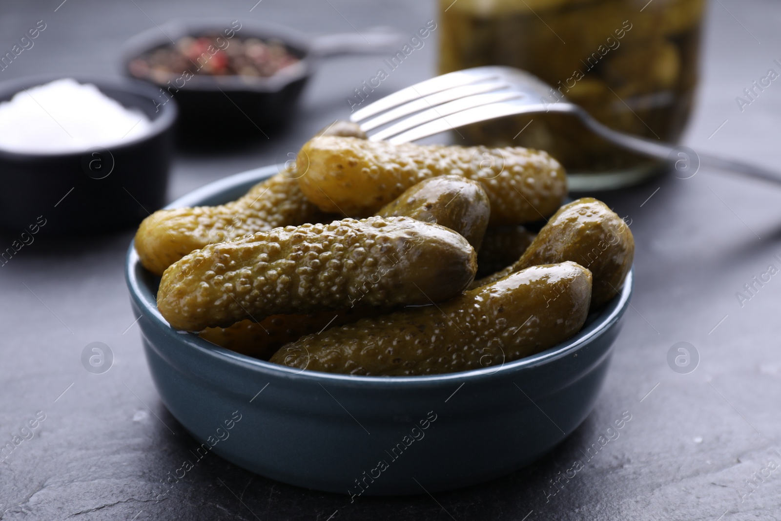 Photo of Bowl of pickled cucumbers and ingredients on black table, closeup