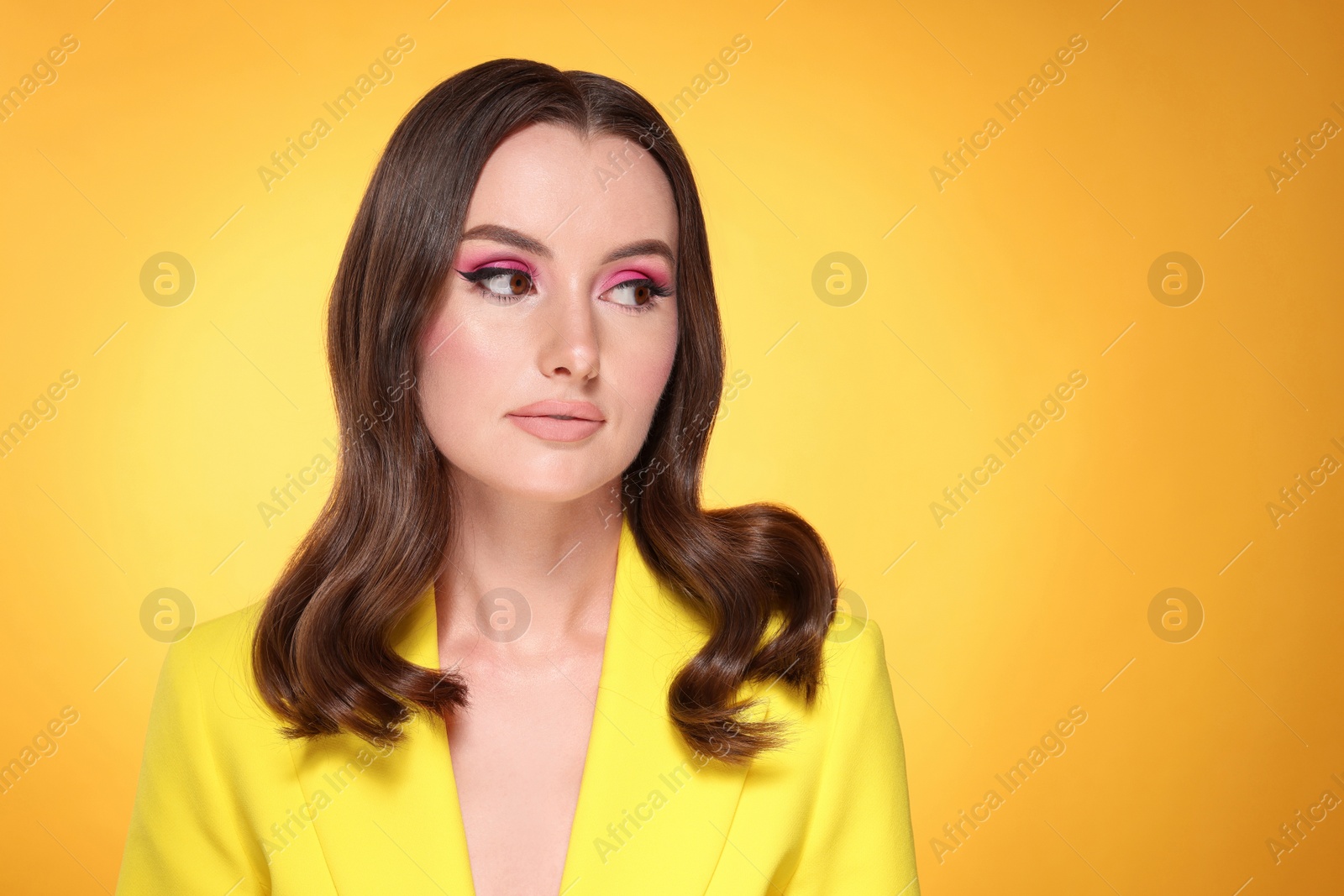 Photo of Portrait of beautiful young woman with makeup and gorgeous hair styling on yellow background. Space for text