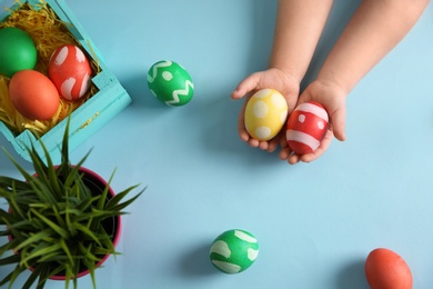 Little child holding painted Easter eggs on color background, top view