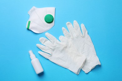 Hand sanitizer, medical gloves and respirator on light blue background, flat lay