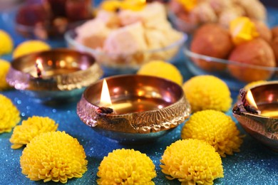 Photo of Diwali celebration. Diya lamps and chrysanthemum flowers on shiny light blue table, closeup